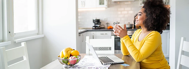 Woman in yellow sweater sitting at kitchen table with laptop
